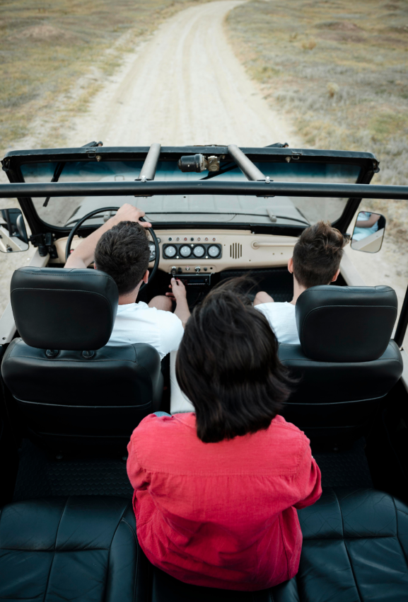 Three friends driving an open jeep on a dirt road